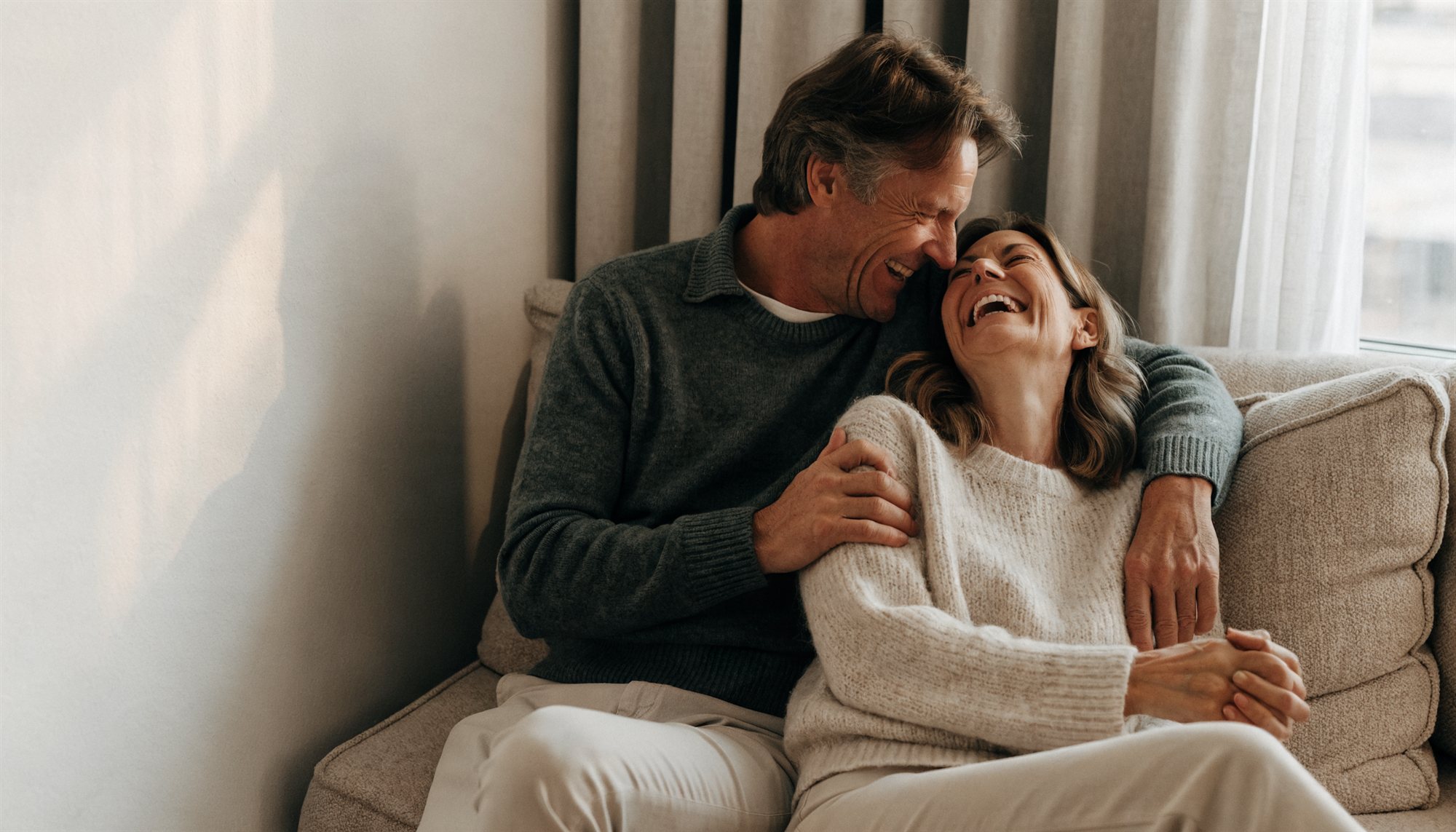 Couple laughing together on a couch at home