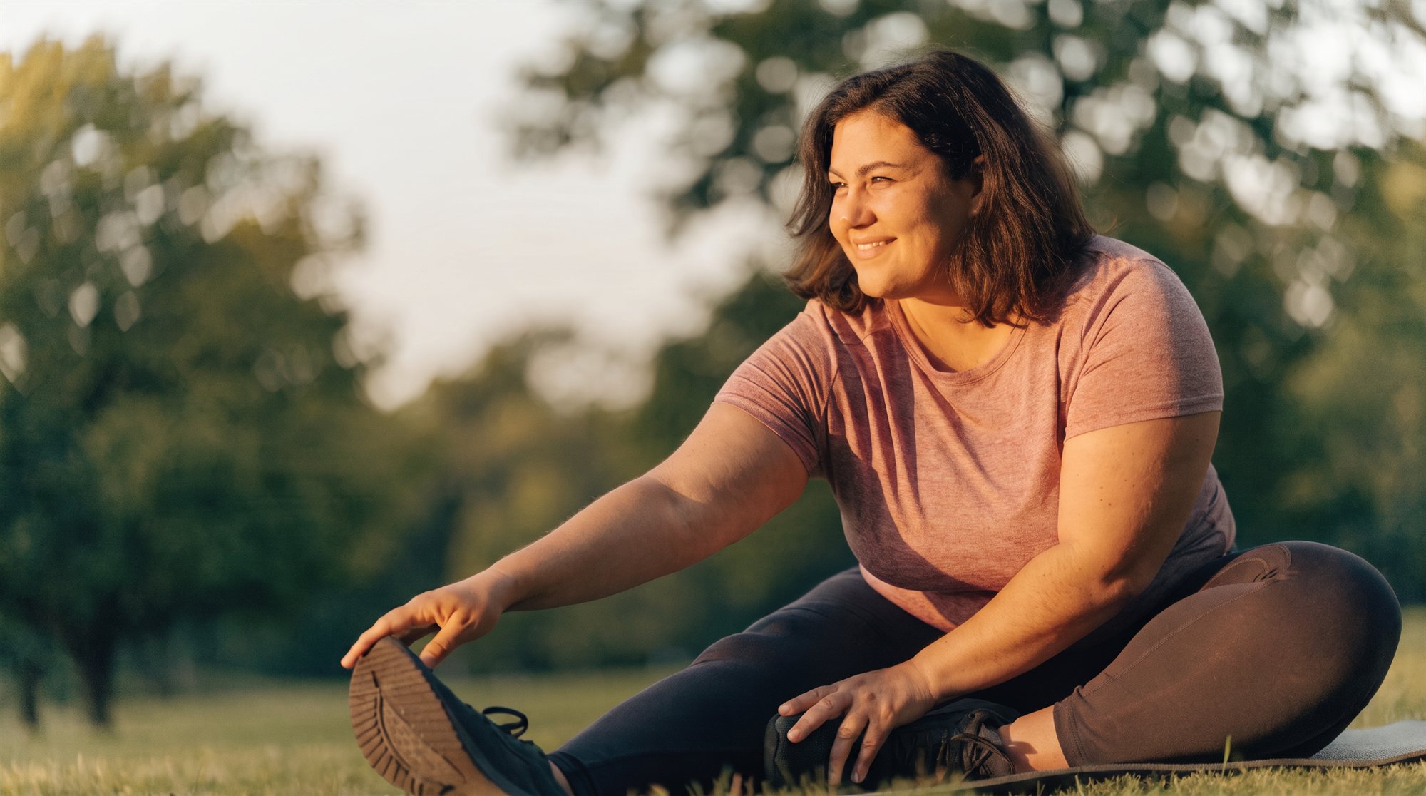 Woman stretching on a yoga mat in a park at golden hour